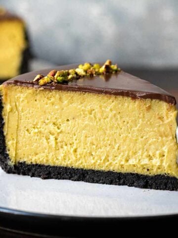 A plate with a slice of pistachio cheesecake with chocolate crust and chocolate topping.