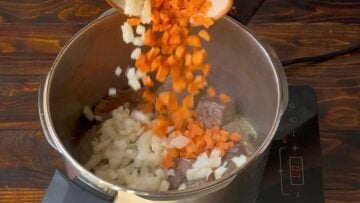 A hand adding chopped carrot and onion to the pot.
