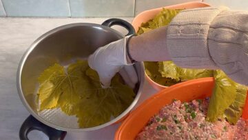 Two hands layering grape leaves at the bottom of the pot.