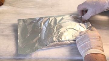 Two hands wrapping the leaves with aluminum foil.