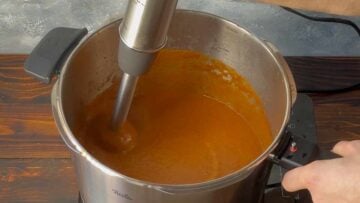 An immersion blender blending the tomato sauce.