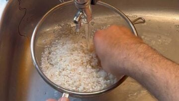 A hand rinsing rice in a sieve.