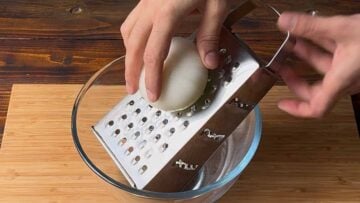 A hand grating an onion on a box grater.