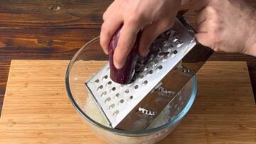 A hand grating an eggplant on a box grater.