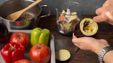 A hand scraping the flesh from the inside of an eggplant.