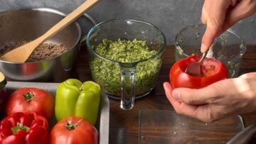 A hand hollowing out a tomato with a spoon.