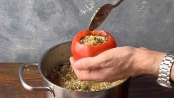 A hand filling a tomato with the rice mixture.