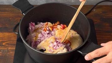 A wooden spoon stirring the vegetables with the chicken.