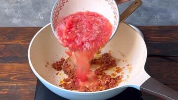 A hand pouring rated tomatoes in the pan.