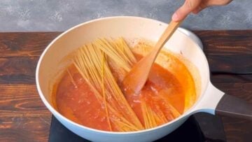 Spaghetti in a pan with tomato sauce.