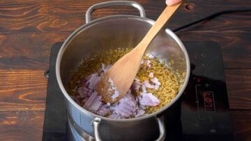 Bulgur, onion and olive oil in a pot and a wooden spoon.