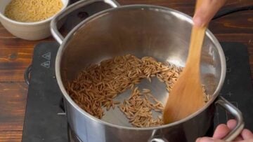Orzo pasta in a pot with olive oil and a wooden spoon.