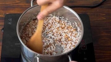 A hand stirring orzo pasta and rice in a pot.