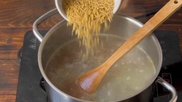 A hand adding orzo to a pot with boiling water.