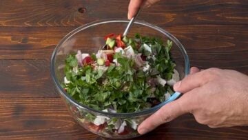 A hand mixing orzo pasta salad in a bowl with a spoon.