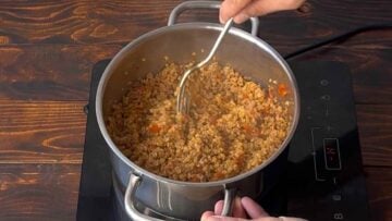 A hand fluffing cooked bulgur with a fork.