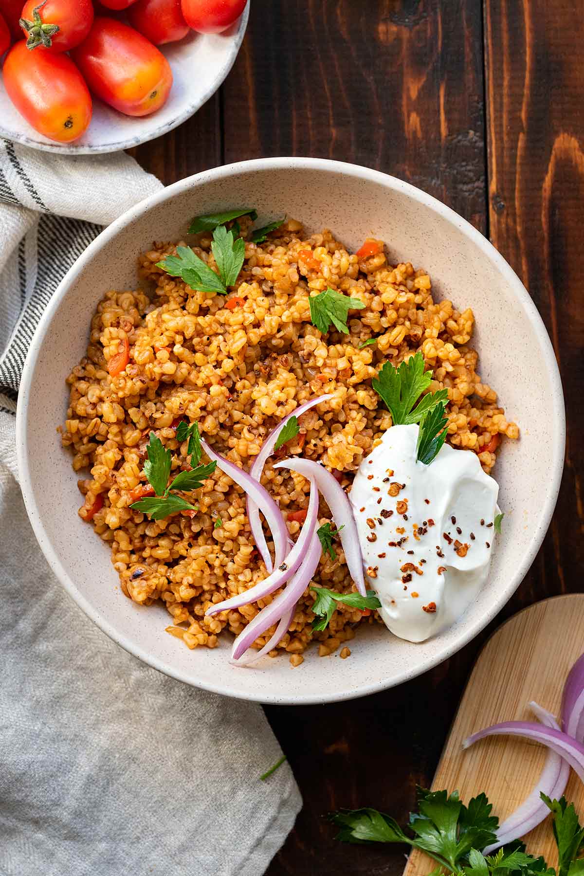Bulgur pilaf in a bowl with yogurt, onion slices and parsley.