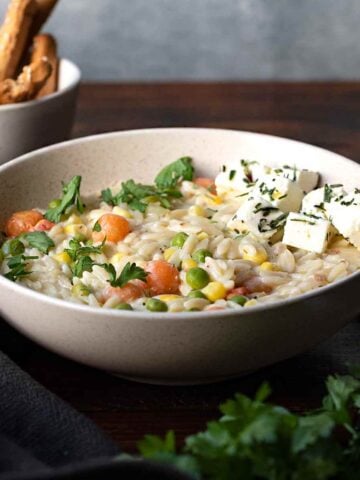 Creamy orzo pasta with vegetables and feta cheese in a bowl.
