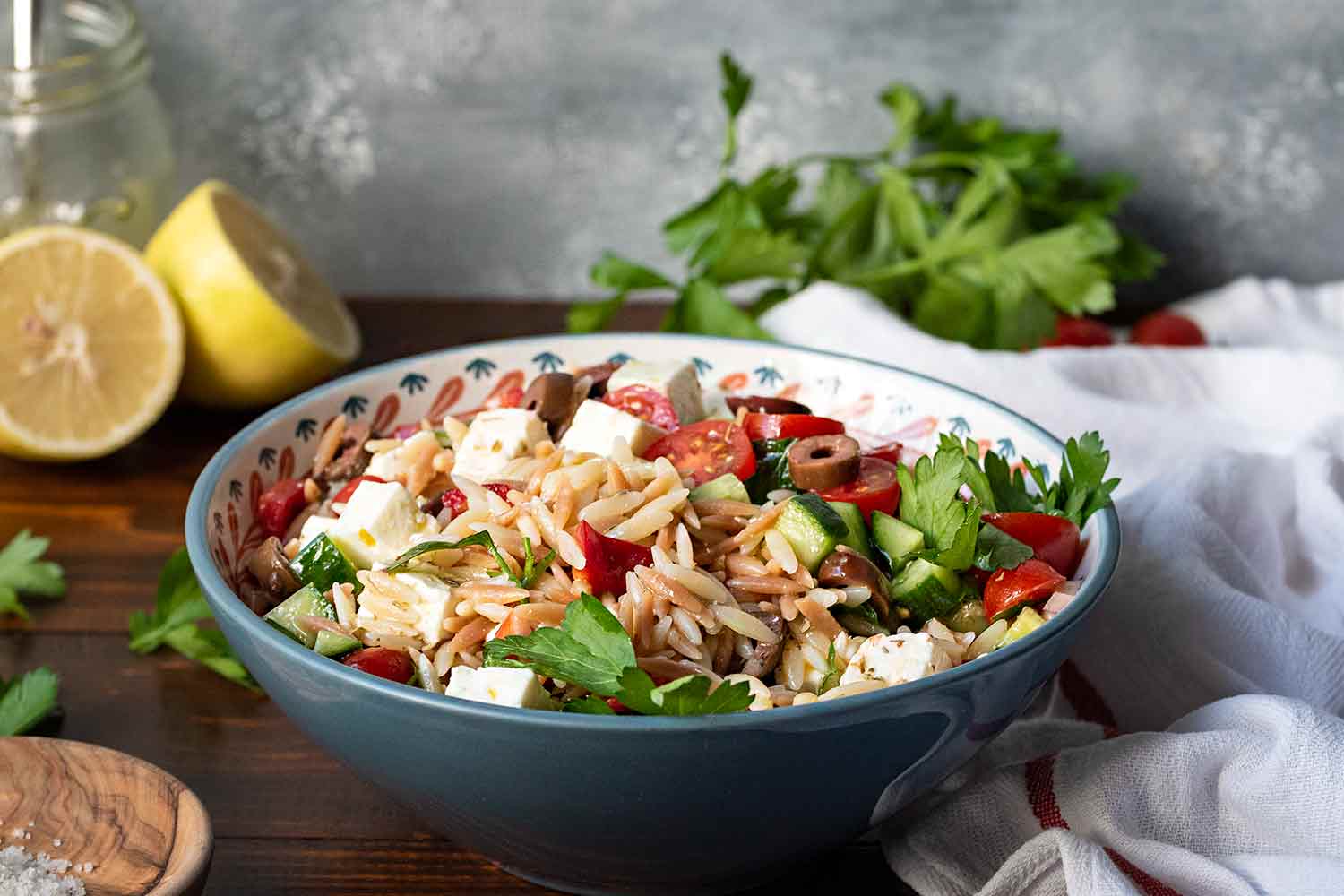 Orzo salad served in a bowl with lemon vinaigrette on the side.