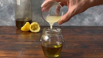 A hand pouring lemon juice to a jar with olive oil.