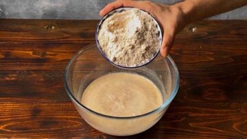 A hand adding barley flour to the yeast mixture.