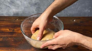 A hand placing bread dough in a bowl.