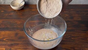 A hand adding flour to the proofed yeast mixture.