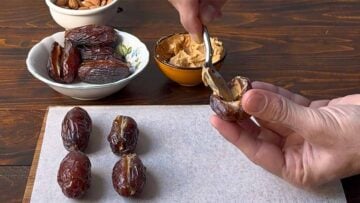 A hand stuffing a date with peanut butter.