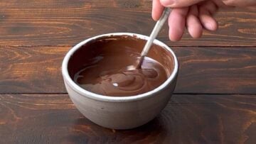 A hand stirring melted dark chocolate with a spoon.