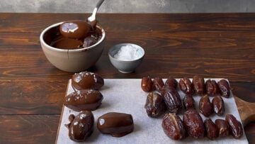 A hand dipping a stuffed date in a bowl with melted chocolate.