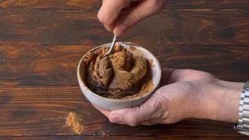 A hand stirring date paste with ground cinnamon.