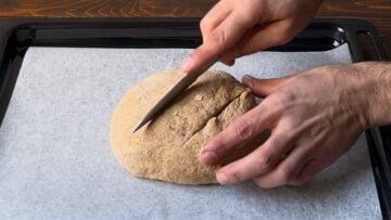 A hand scoring a loaf with a knife.