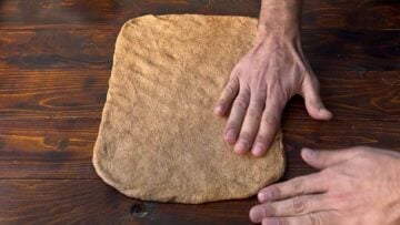 Two hands spreading the dough into a rectangle.