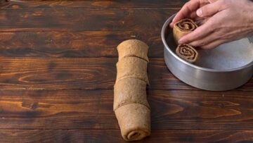 Two hands placing the cinnamon buns in a baking pan.