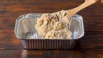 Bread dough made with barley in a baking pan and a wooden spoon.