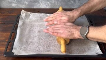 Two hands flattening the dough with a rolling pin.