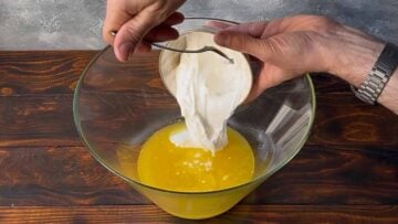 Two hands add yogurt to a bowl with melted butter.