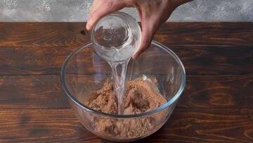A hand pouring water into a bowl with cacao powder.