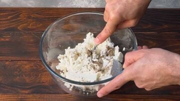 A hand crumbling feta into a bowl with a fork.