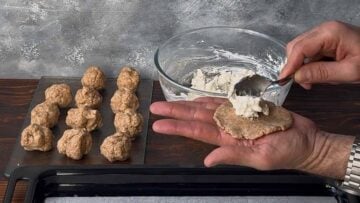 A hand adding feta filling to the dough.