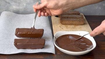 A hand dipping the bars into melted chocolate.