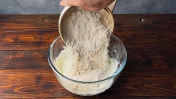 A hand adds flour to a bowl with Greek yogurt.
