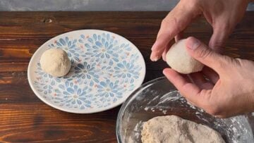A hand dividing the flatbread dough into balls.