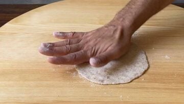 A hand rolling the dough into discs.