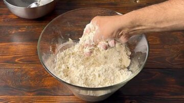 A hand rubbing flour with olive oil in a bowl.