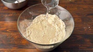 A hand pouring water in the bowl with the flour.