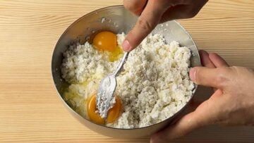 A hand mixing feta, cream cheese and eggs in a bowl with a fork.