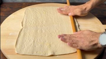Two hands rolling out phyllo with a rolling pin.