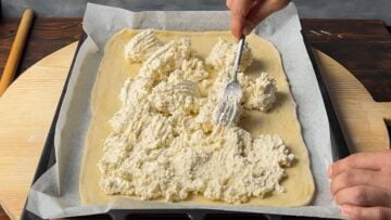 A hand spreading the feta filling on a sheet of Greek phyllo dough.