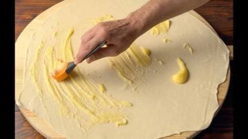 A hand brushing the phyllo sheet with butter.